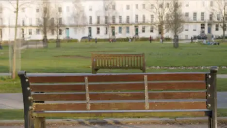 Close Up Shot of Empty Park Bench as People Walk In Background