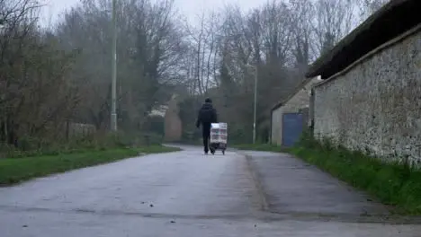 Wide Shot of Person Pulling Sack Truck Down Rural Town Footpath