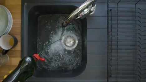 Top Down Shot of Male Hands Pouring Washing Liquid into Sink Under a Running Tap