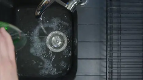 Top Down Shot of Male Hands Pouring Washing Liquid into Sink Under Running Tap