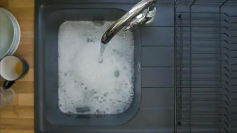 Top Down Shot of Male Hand Mixing Soapy Water In Sink