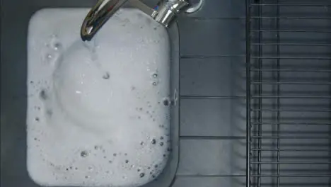 Top Down Shot of Male Hand Turning Off Running Tap as Sink Fills with Soapy Water