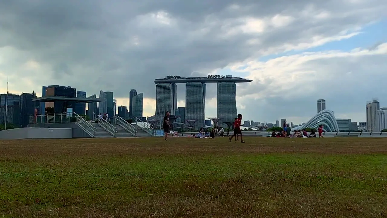 A footage shot of a boy running after a ball in an open field with Marina Bay Sand Hotel Singapore in the backgound