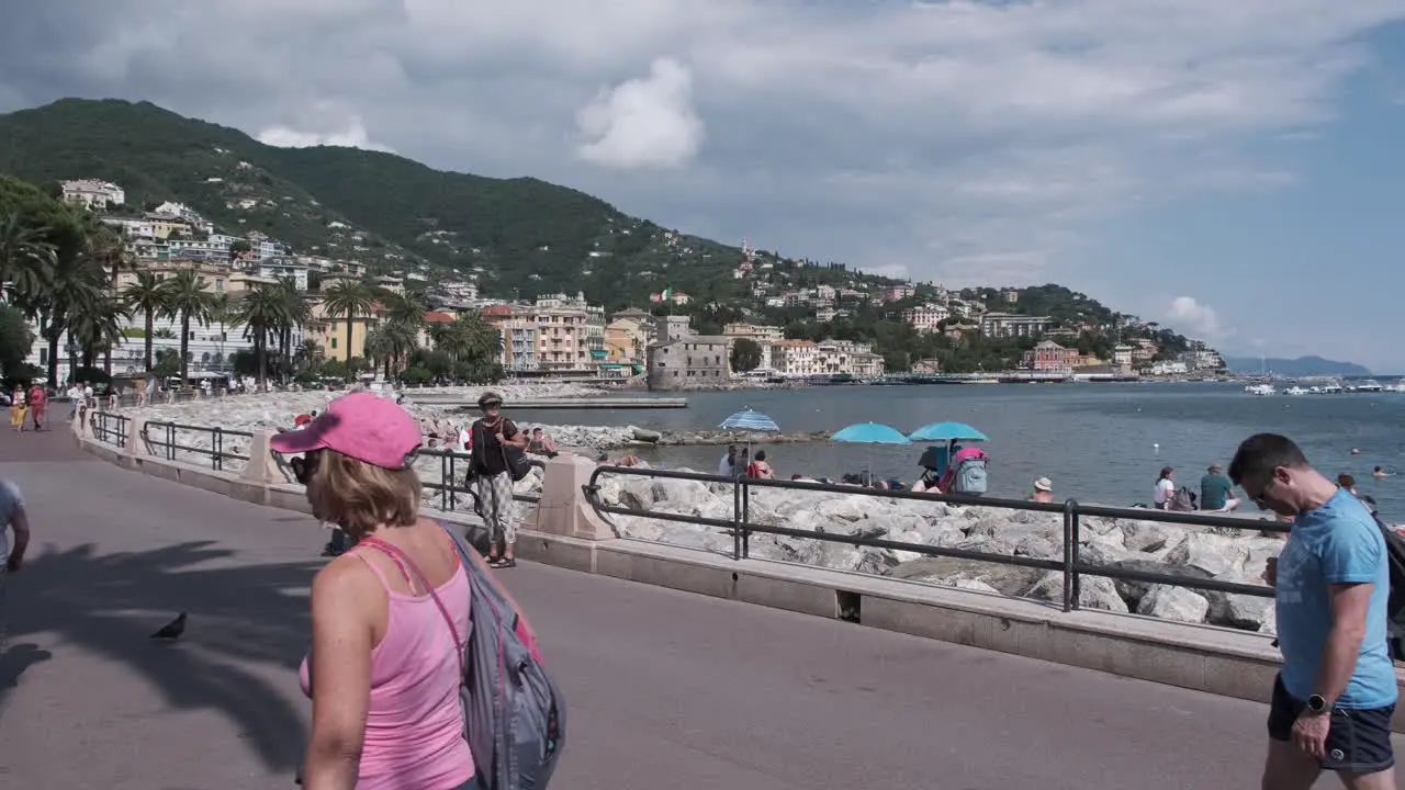 People walking on promenade in Rapallo Italy while others sunbathing on the beach