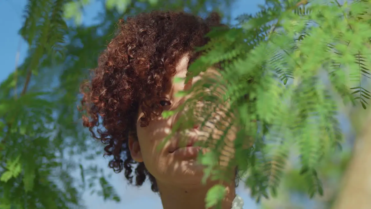 Light skin red hair girl facial close up with leaves in the foreground on a sunny day in the park