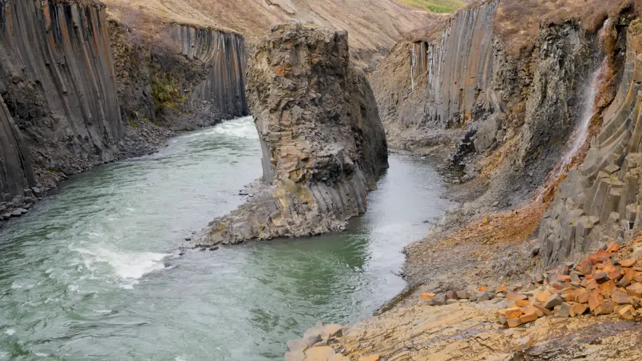 Rushing river flows through a dramatic Icelandic canyon with distinctive basalt column formations and rugged terrain showcasing nature's power