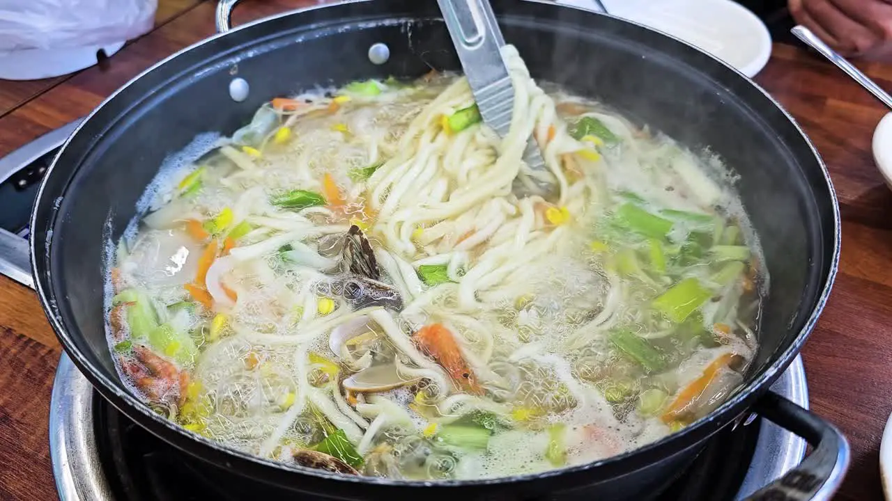 Tongs Mix Knife Cut Noodle Soup While Cooking Seafood Clam Kalguksu Boiling in Pot