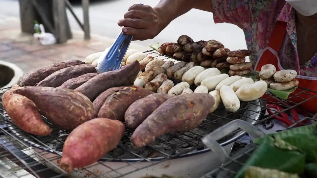 Close up of female hand turning sweet potatoes while baking above hot embers