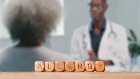 Medical Concept With Wooden Letter Cubes Or Dice Spelling Allergy Against Background Of Doctor Talking To Patient In Hospital