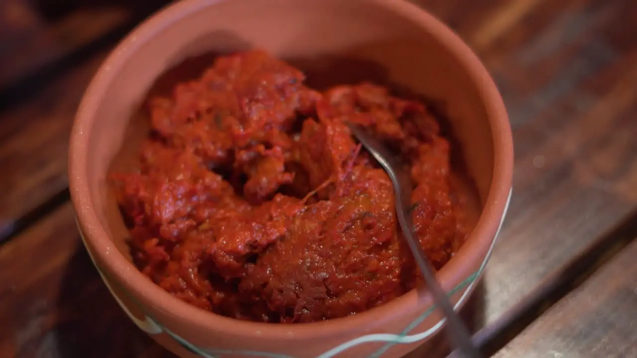 Ajvar in earth jar with little spoon on a wooden desk