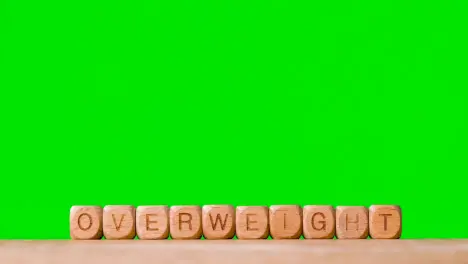 Medical Concept With Wooden Letter Cubes Or Dice Spelling Overweight Against Green Screen Background