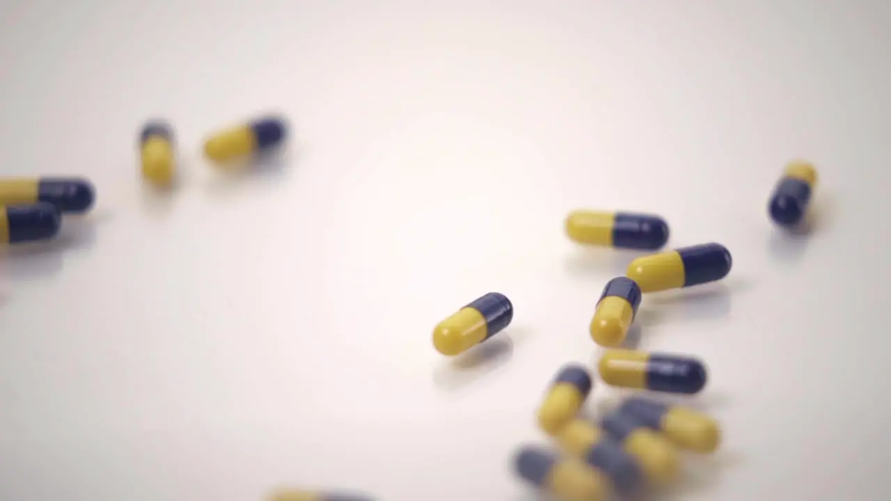 Slow Motion Macro of Blue and Yellow Pills Pushing One Yellow Pill Out of Frame on White Background