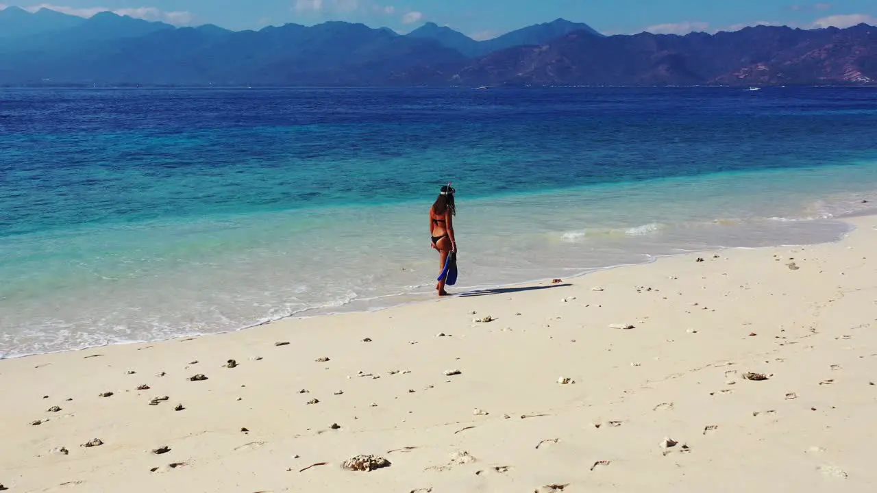 Woman walking through the shallow ocean waves by herself down a beautiful beach shoreline