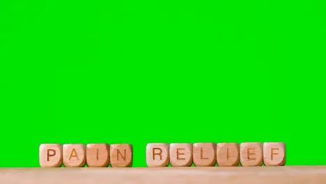 Medical Concept With Wooden Letter Cubes Or Dice Spelling Pain Relief Against Green Screen