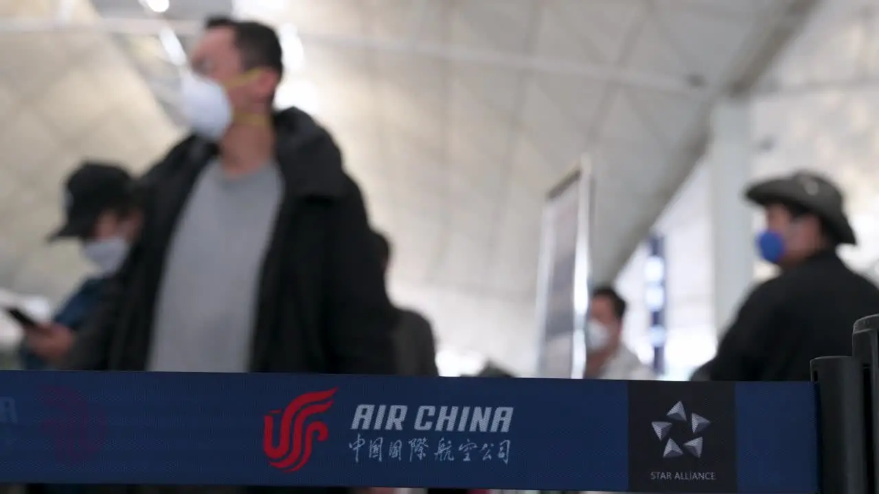 Chinese flag carrier Air China airline logo is seen on a queue belt in the foreground as flight passengers line up at a check-in desk counter at the Chek Lap Kok International Airport in Hong Kong