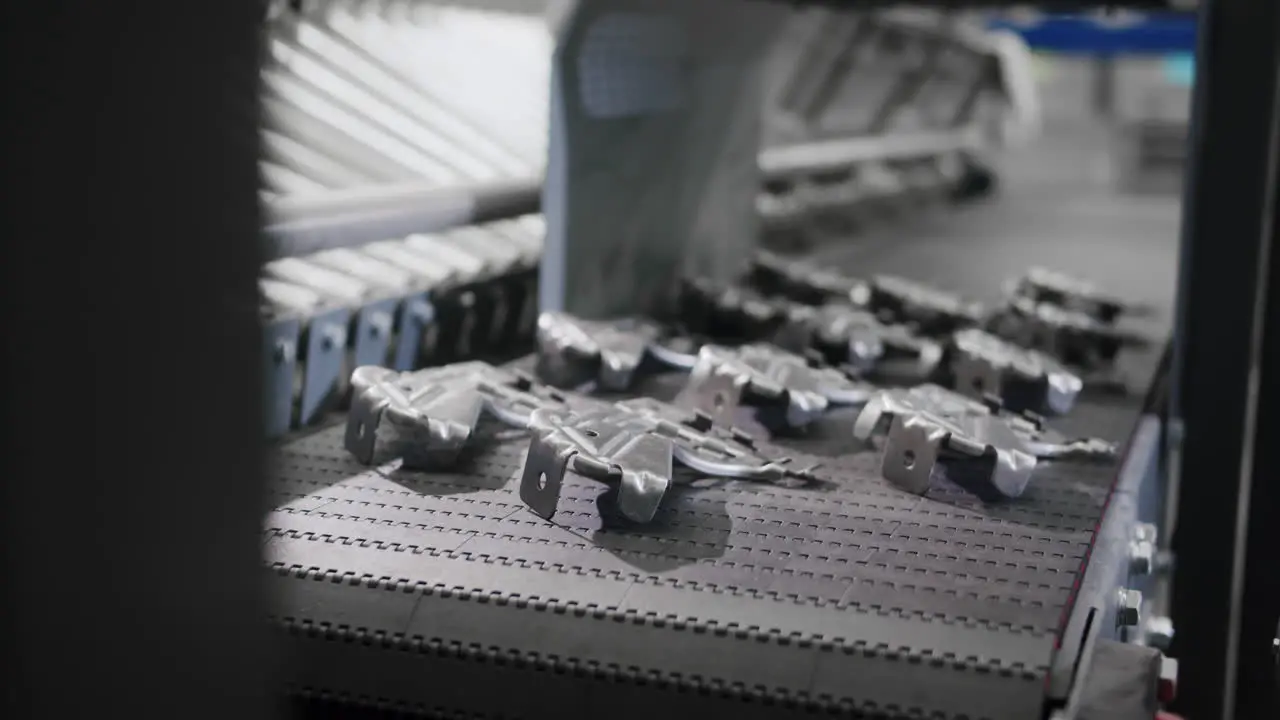 Close up of an automated robotic arm taking a raw metal car part from a conveyor belt and transferring it to the next stage in the production factory