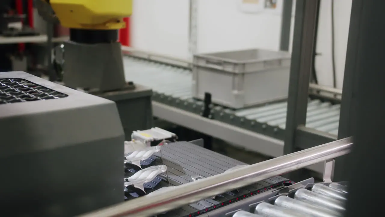 Medium shot of a yellow automatized robotic arm taking a metal car part from the conveyor belt and taking it to the next step in the production line factory