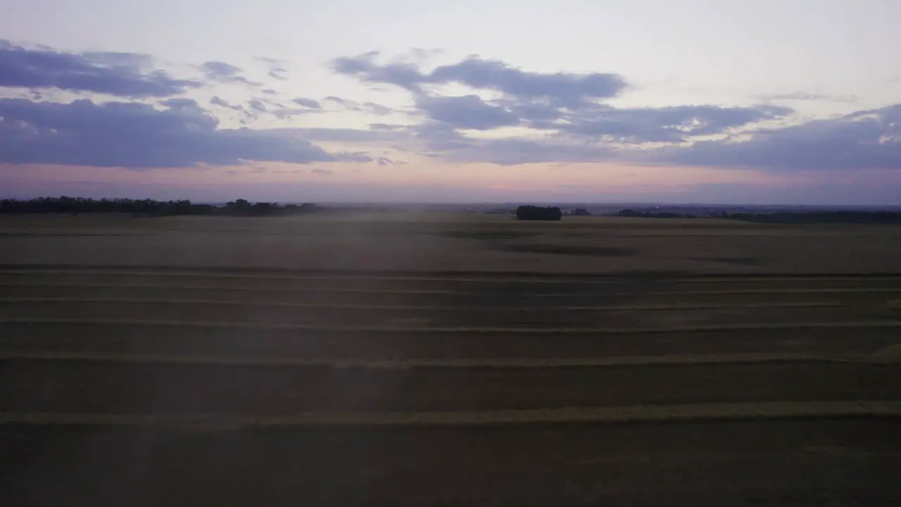 Fast low drone flight over combine harvester harvesting grains at twilight