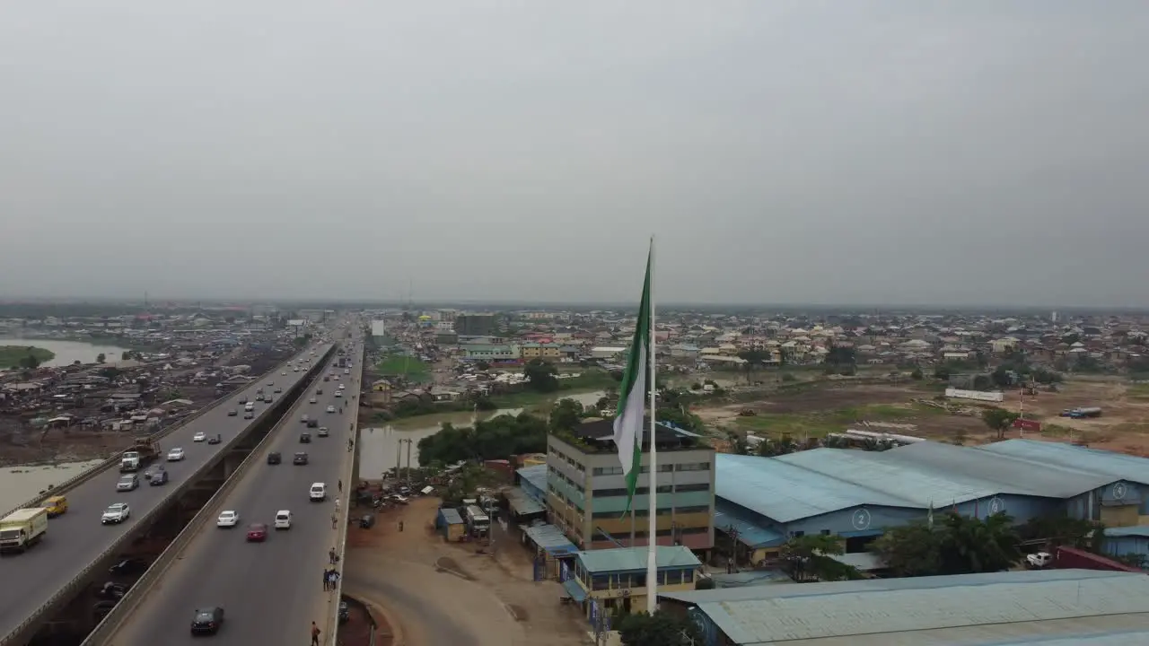 Cars moving speedily on bridge of a sub-urban highway with a Nigerian flag in front of an industry