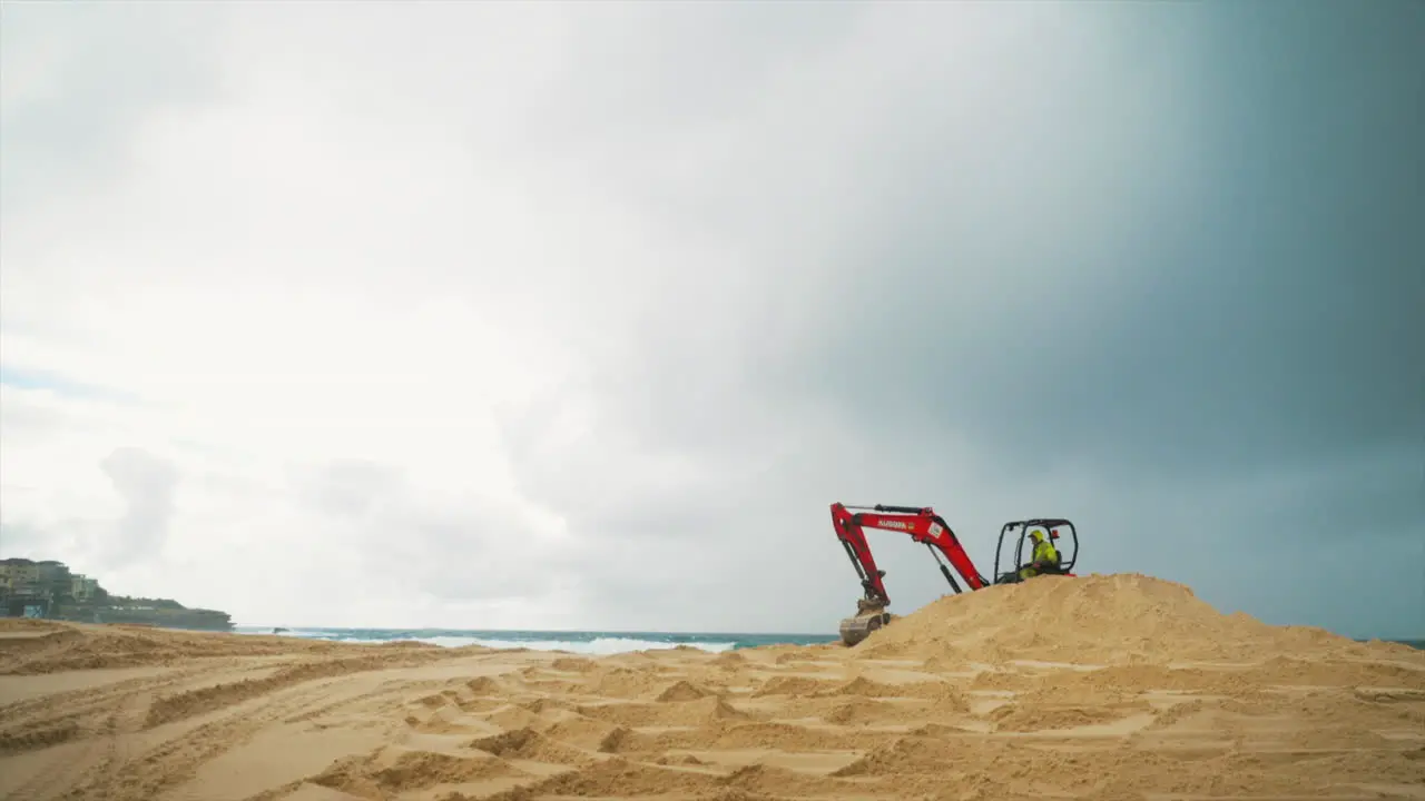 An orange construction excavator scoops and drops sand on a beach by the ocean in Sydney Australia