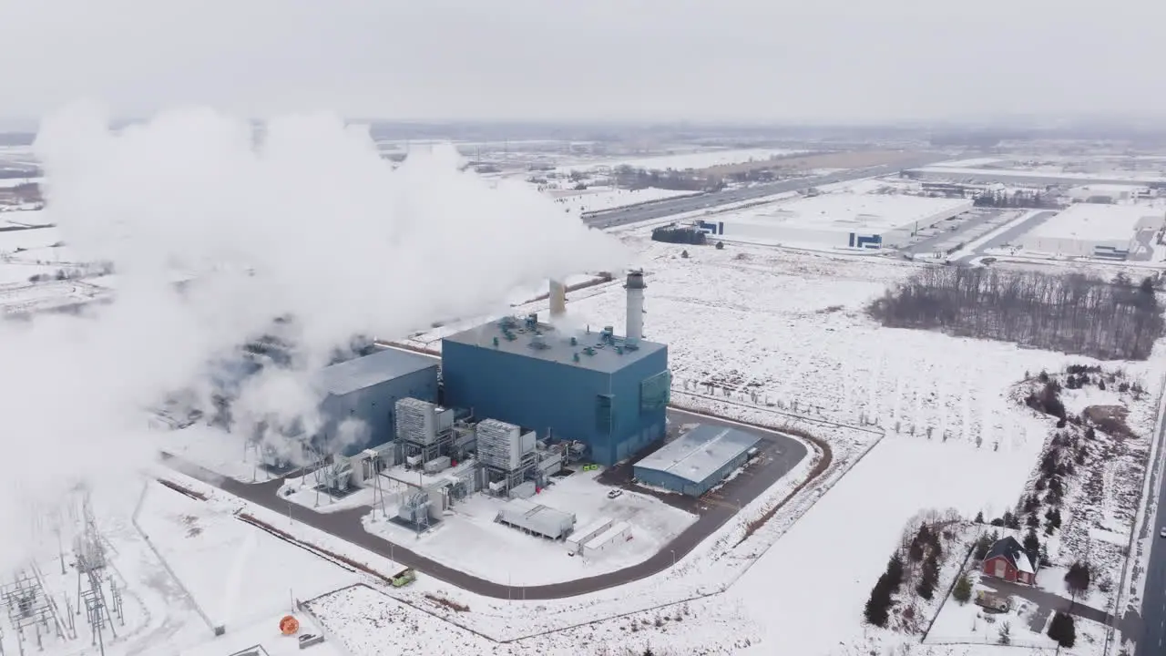 A large industrial plant emitting steam in a snowy landscape winter aerial view