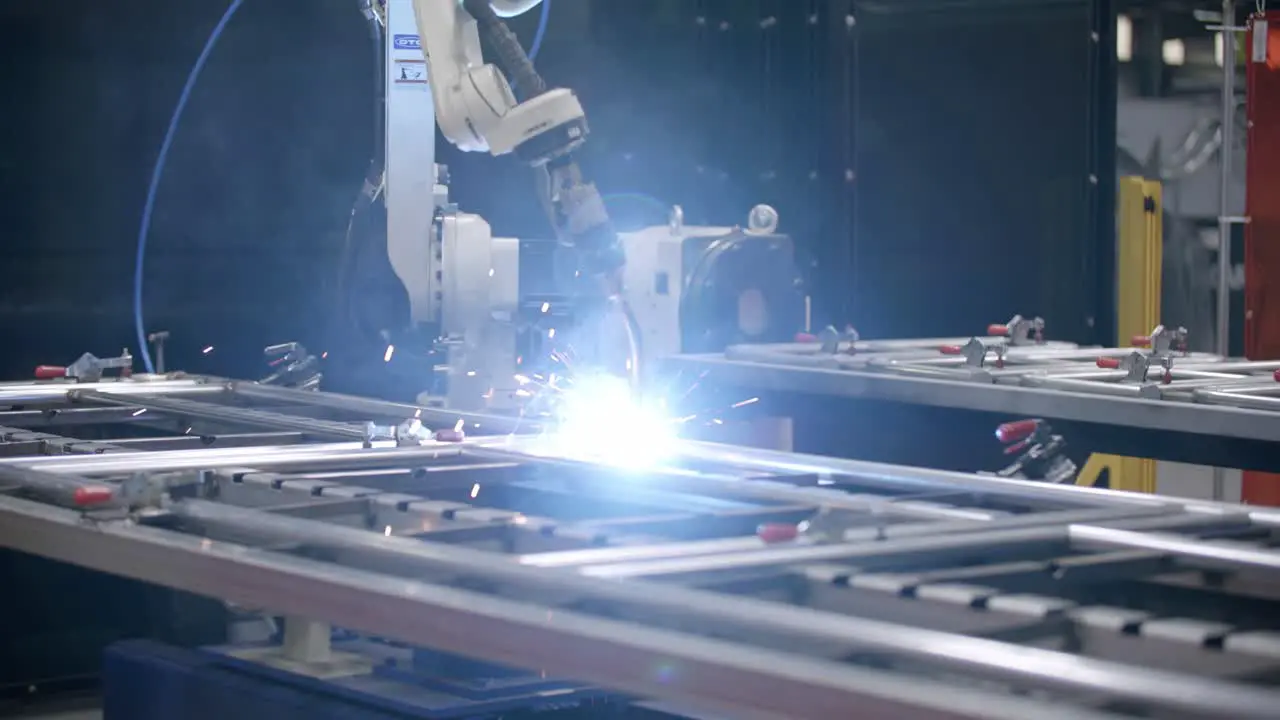 Wide slow motion footage of a robotic welder with bright fire and sparks putting a weld on a steel frame