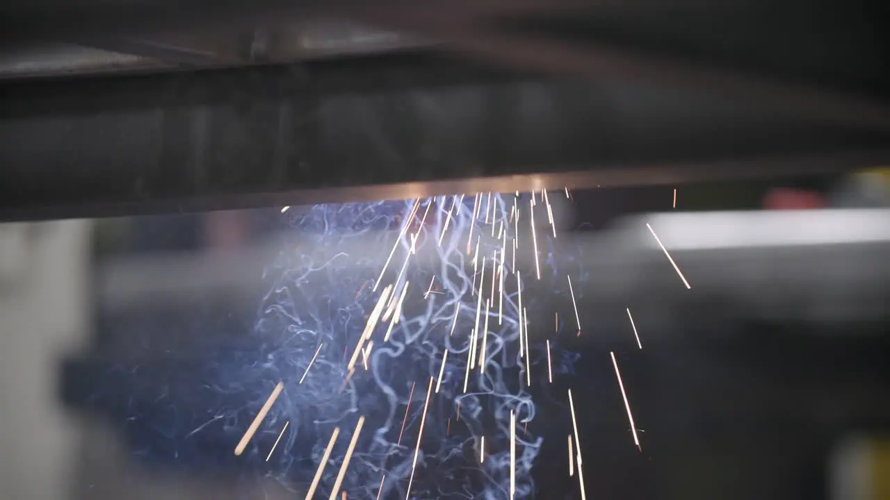 Slow motion footage of sparks and smoke flying out from under a steel frame that is being welded