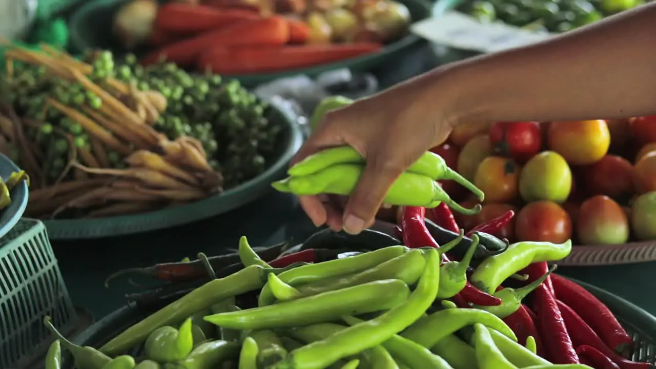 A close up shot of a girl choosing green chilli peppers in a street market in Thailand south-east asia