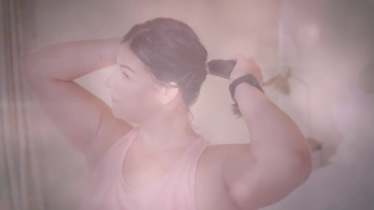 Animation of flickering spots of light over woman tying her hair before exercising at home