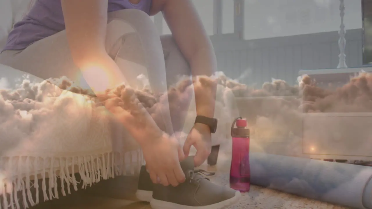 Animation of sunset and clouds over woman tying shoe laces exercising at home