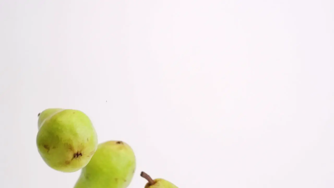 Whole pears falling and bouncing in slow motion on white studio backdrop in 4k