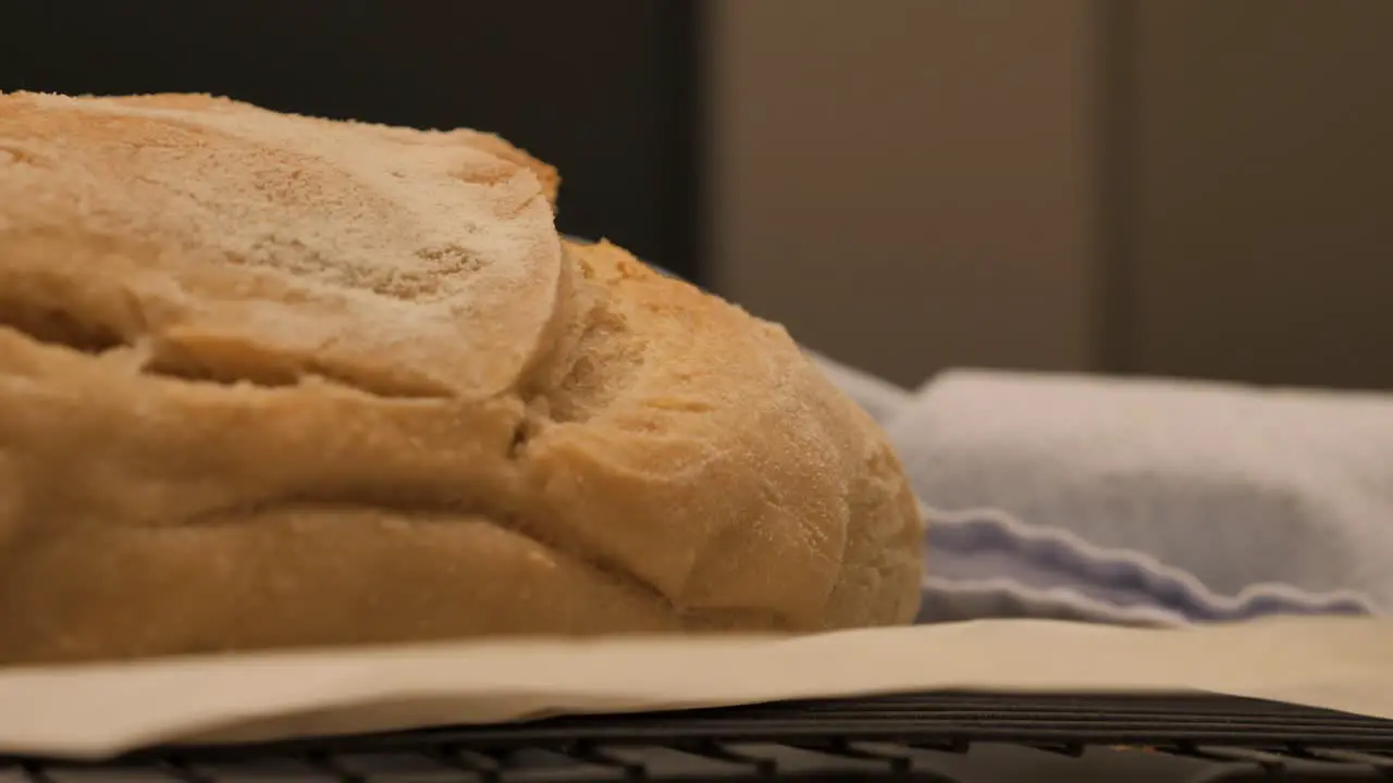 Slow motion pan through to freshly baked loaf of sour dough bread topped with flour sitting on kitchen bench with tea towel and tray low depth of field