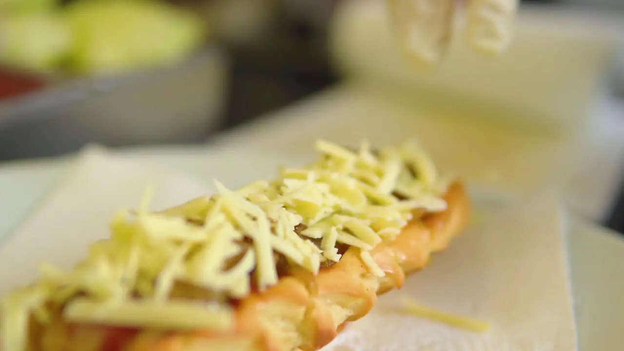 Placing cheese with gloves on top of a hotdog