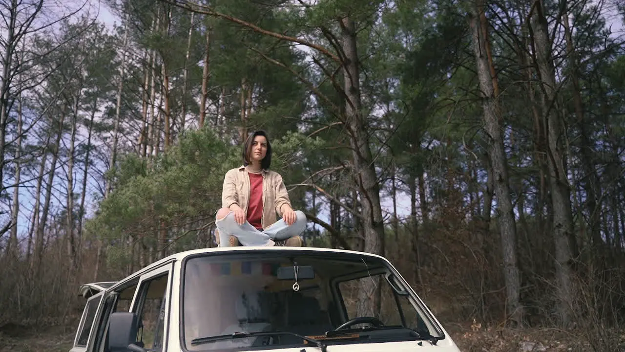 A Pretty Brunette Girl Is Sitting Relaxed On Top Of The Roof Of A Caravan In The Middle Of The Forest