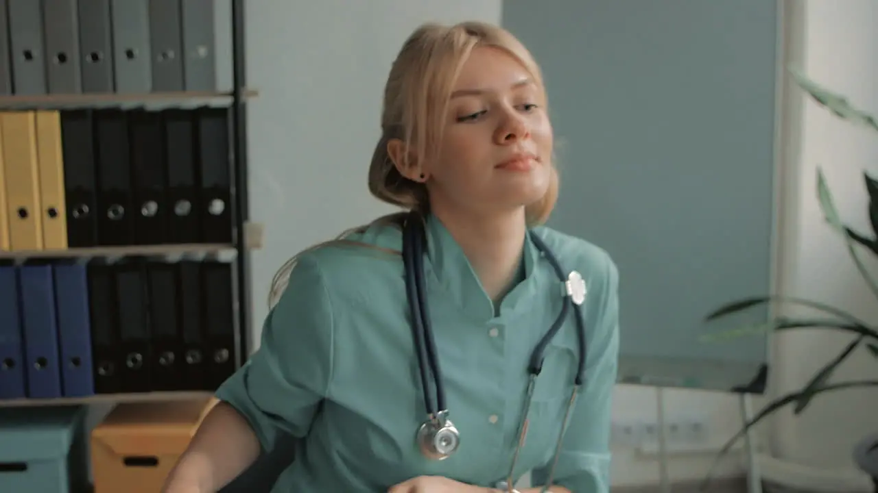 Young Pretty Blonde Female Nurse Care Taker Working At The Office Desk Picking Up Stethoscope And Clipboard