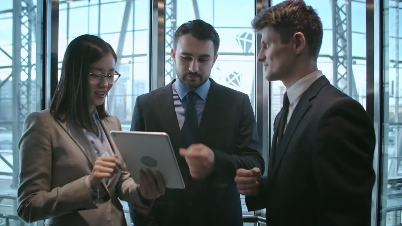 Businesswoman And Two Businessmen In A Elevator Talking And Looking A Tablet 1