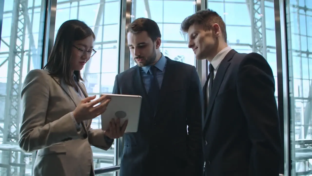 Businesswoman And Two Businessmen In A Elevator Talking And Looking A Tablet