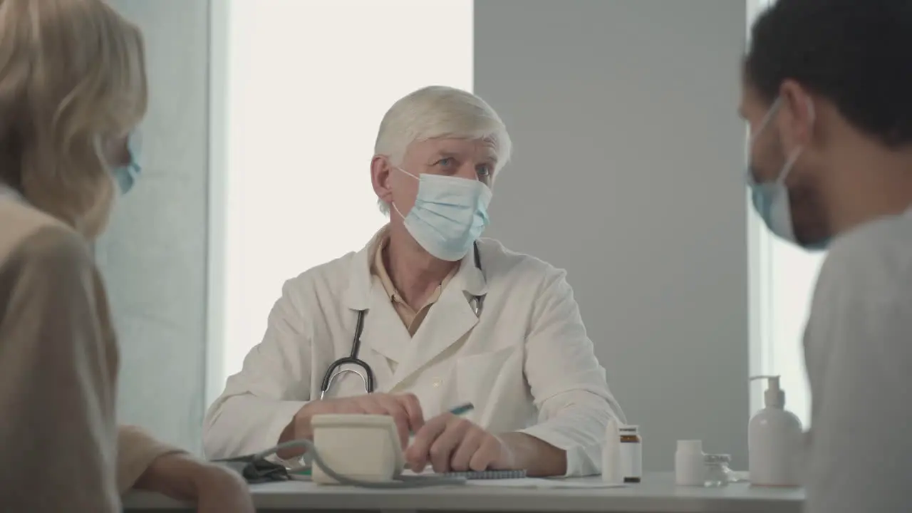 A Grey Haired Middle Aged Doctor In A Facemask Asking Questions To A Young Black Man 1