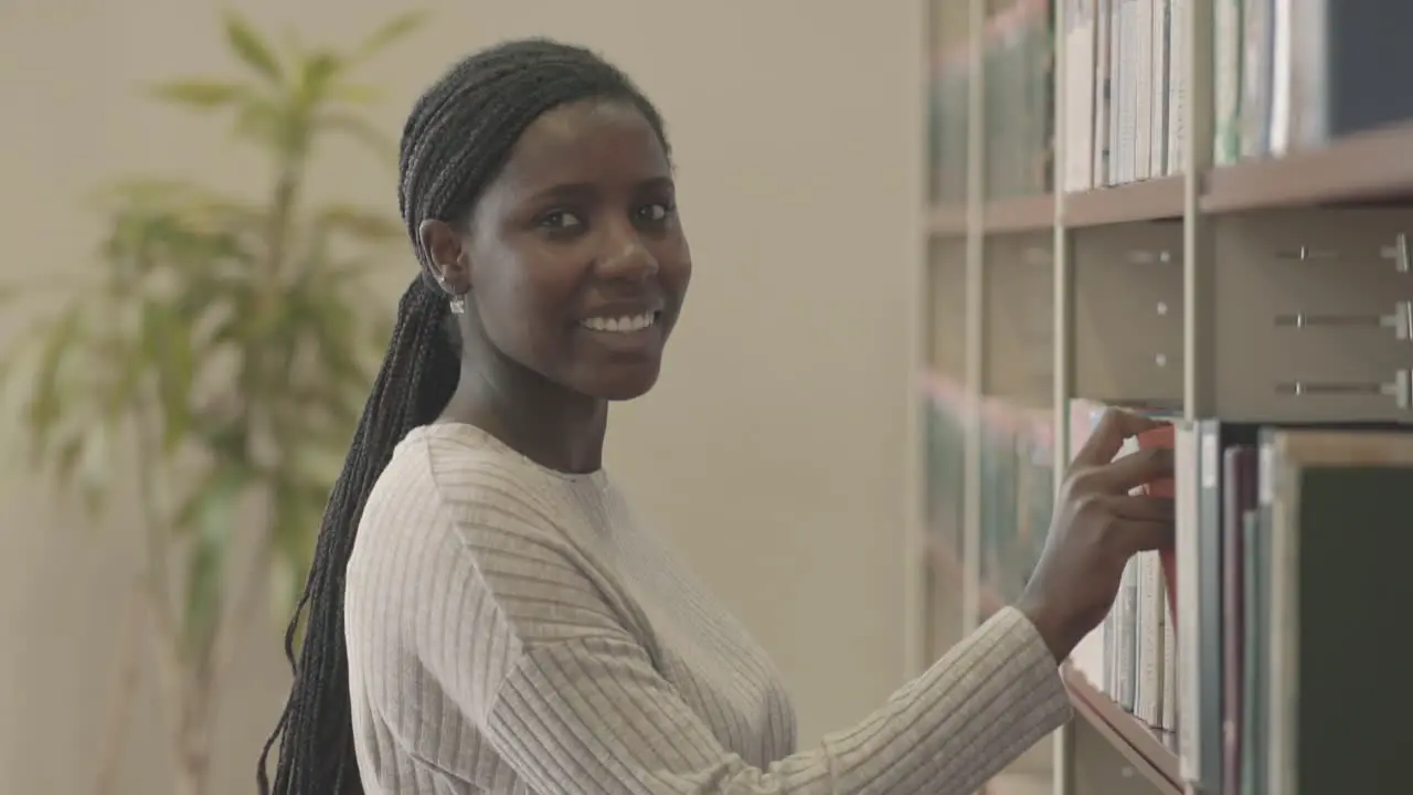 Pretty Black Woman Takes A Book In The Library And Smiles Directly To The Camera