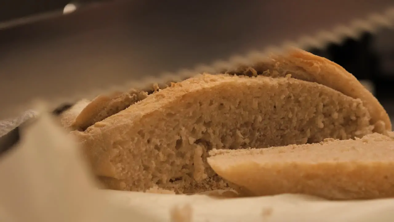 Female hand cutting through final piece of freshly baked sour dough bread with sharp bread knife before placing to side