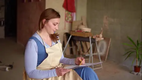 Artist woman at the workplace drawing pencil sketch Long haired woman sitting on the chair at the workplace holding work sheet on knees Calm inspirational work at art studio