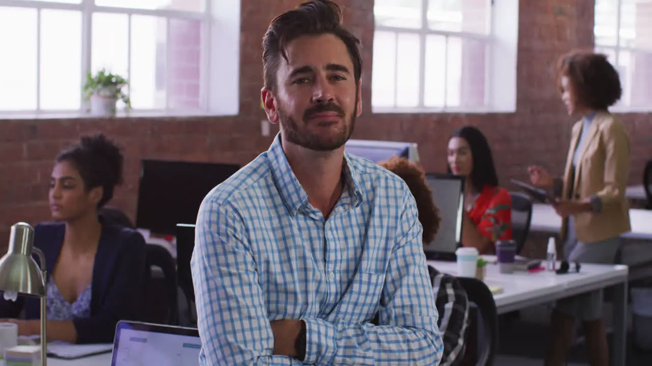 Caucasian businessman sitting smiling in office room with diverse colleagues in background