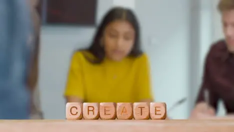 Concept With Wooden Letter Cubes Or Dice Spelling Create Against Background Of People Meeting To Discuss Ideas