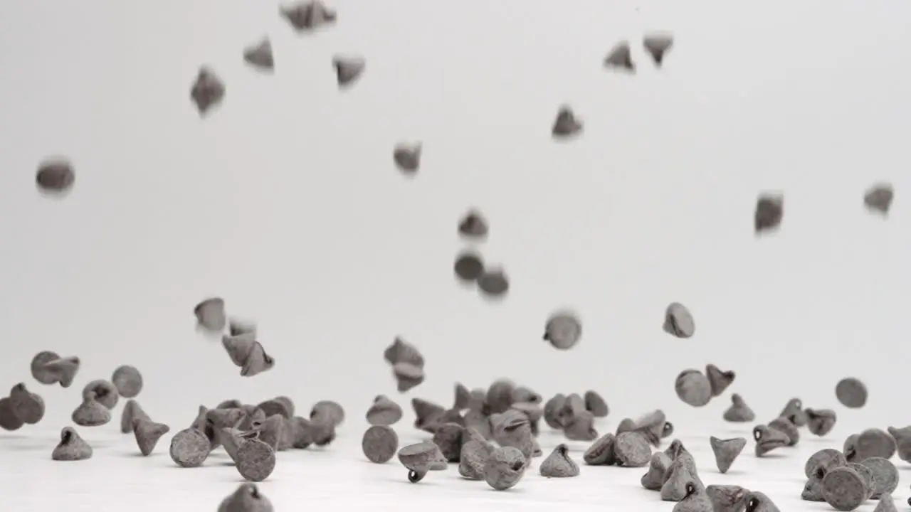 Semi sweet chocolate chips falling and bouncing into pile on white table top in slow motion