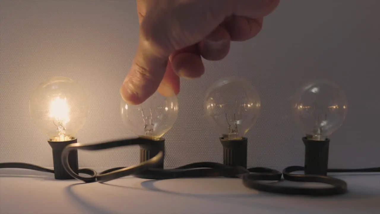 Four filament bulbs being switched on by a hand