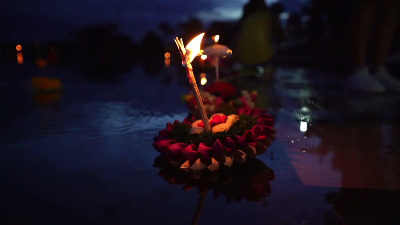 Loy Krathong Festival Colorful Krathong leaning left floating on the dark blue water on the lake with a burning candle and instance on top