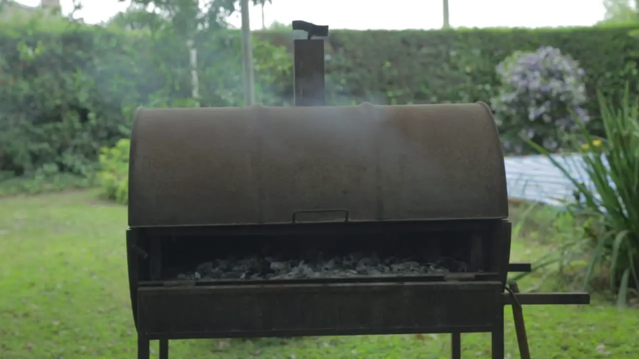 Metal barbecue barrel with smoking coal roasting meat inside in a summer day