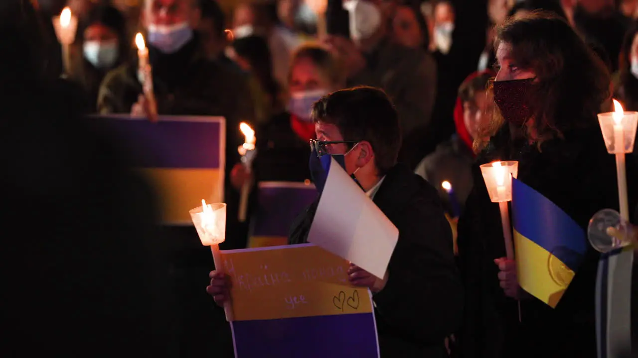 People In Masks Holding Candles And Ukrainian Flags During Prayer Vigil For Peace In Ukraine At Night In Leiria Portugal