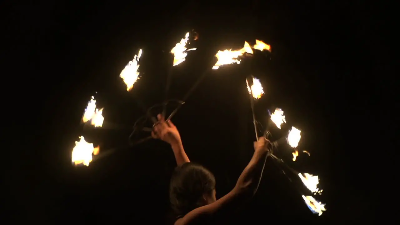 Asian woman spinning brightly lit fire fans with dark background filmed in slow motion as tight close up