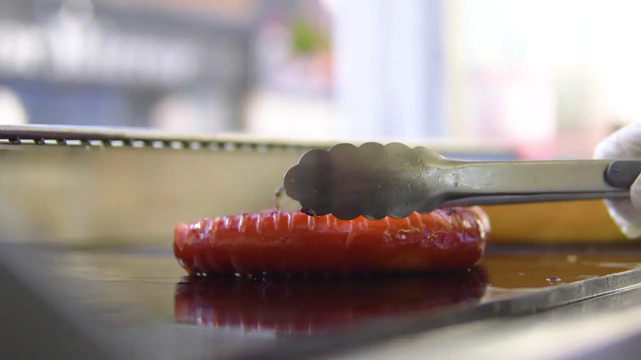 chief cook in open window fast food shop placing sausage on the grill slowmotion